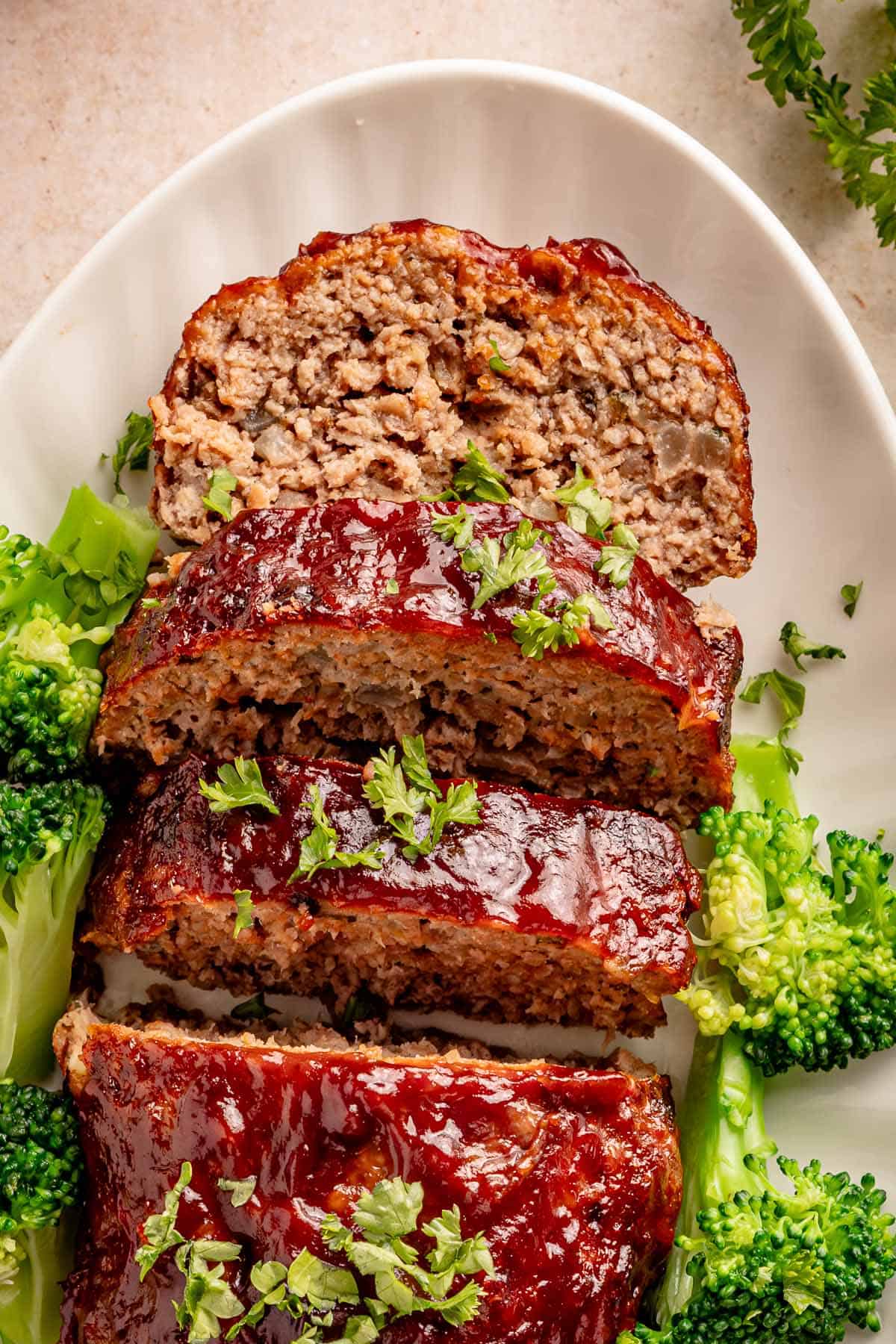 Glazed meatloaf slices with broccoli and parsley on a white plate