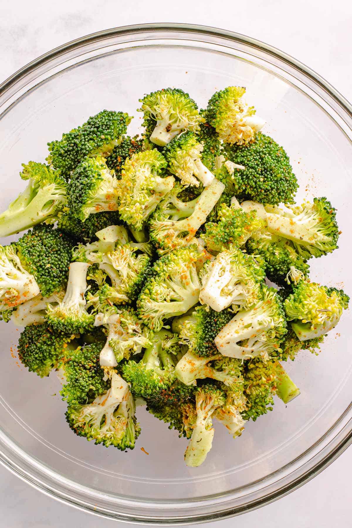Seasoned broccoli florets in a glass mixing bowl