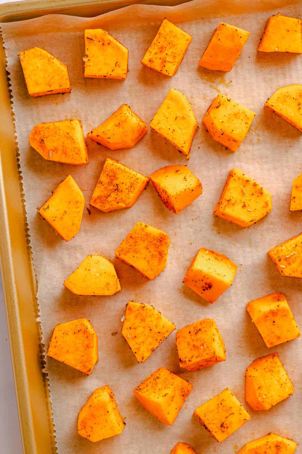 Seasoned sweet potato cubes arranged on a parchment-lined baking sheet
