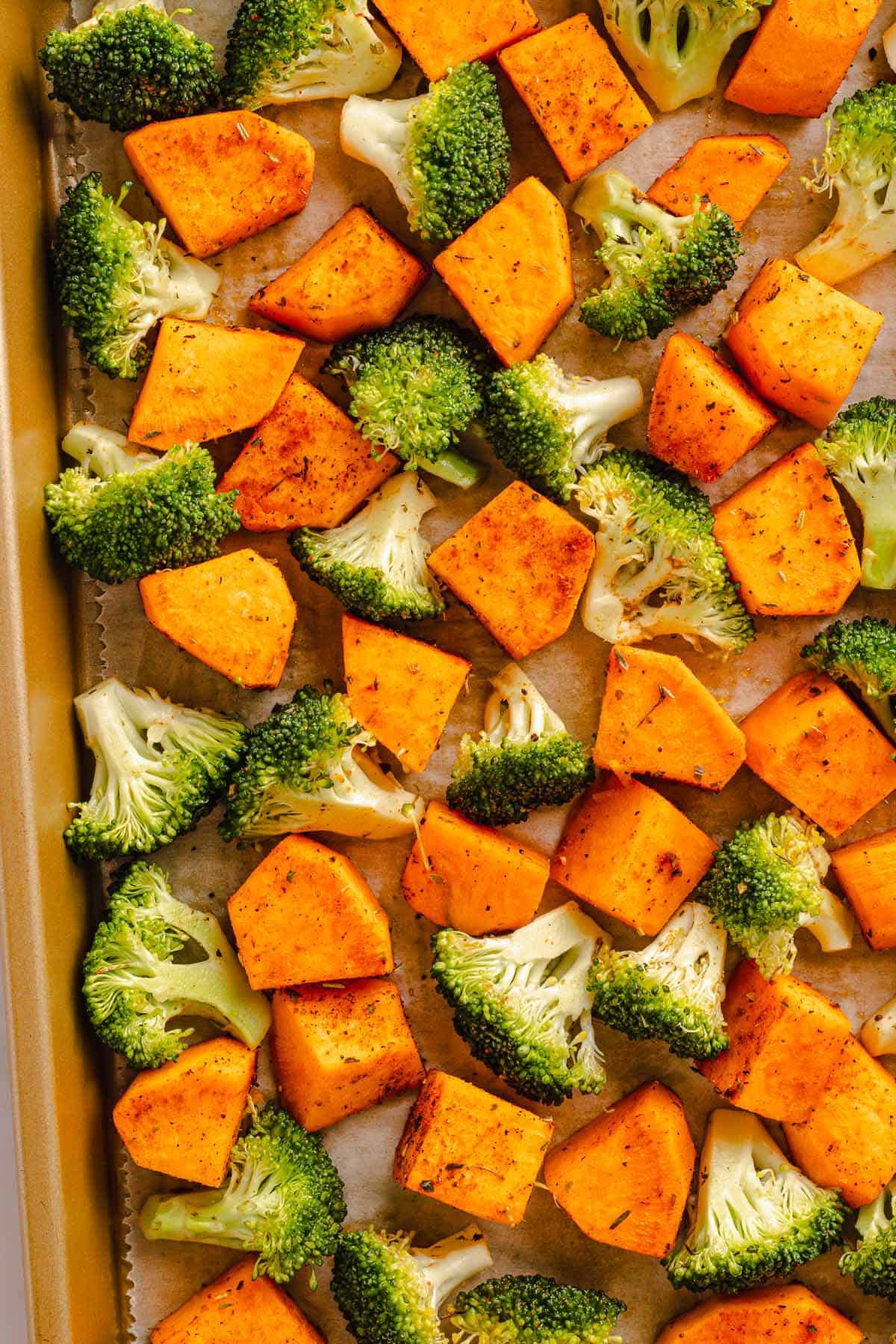 Broccoli and sweet potatoes spread on a sheet pan before roasting