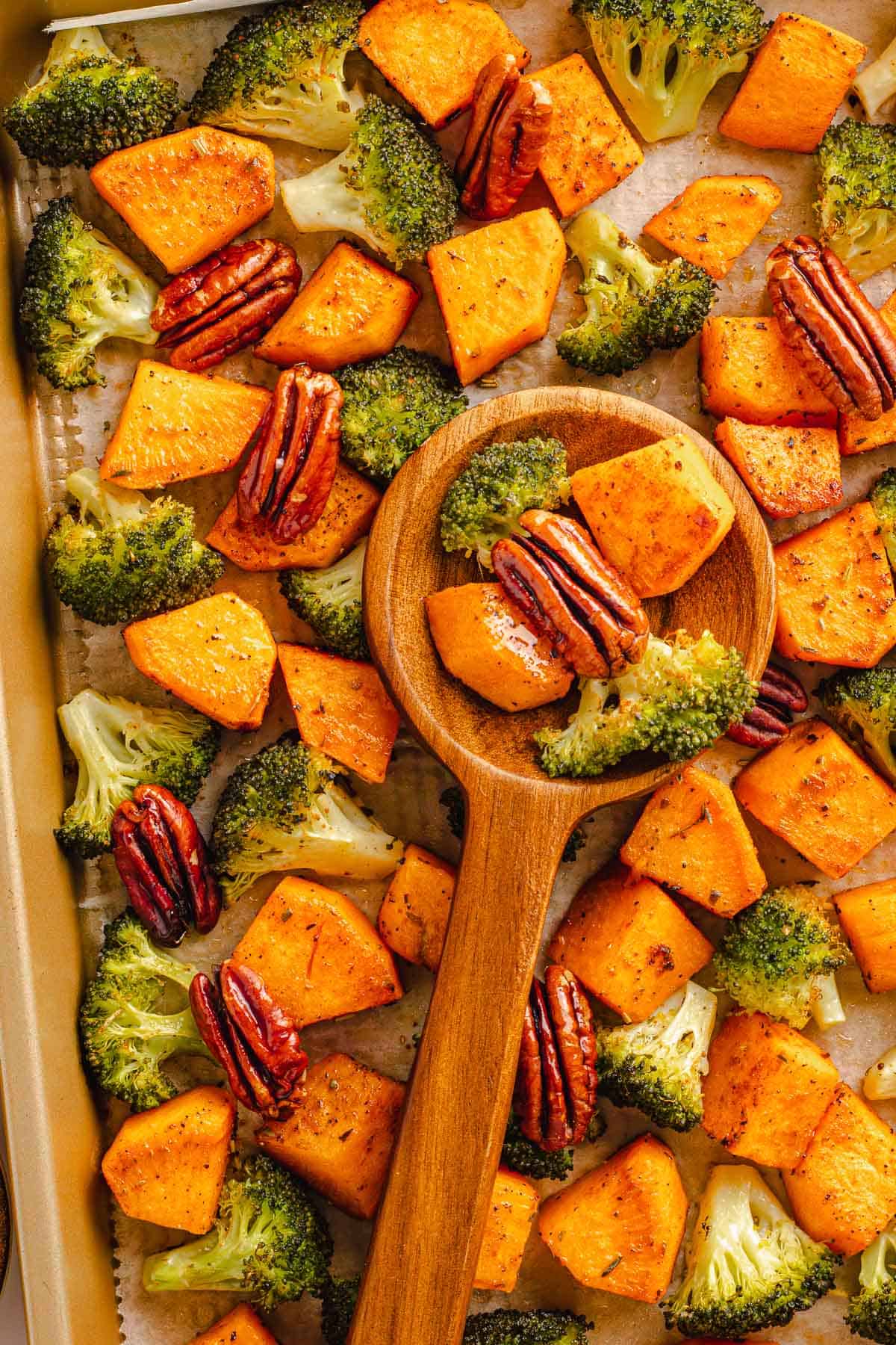 Wooden spoon scooping roasted broccoli, sweet potatoes, and pecans