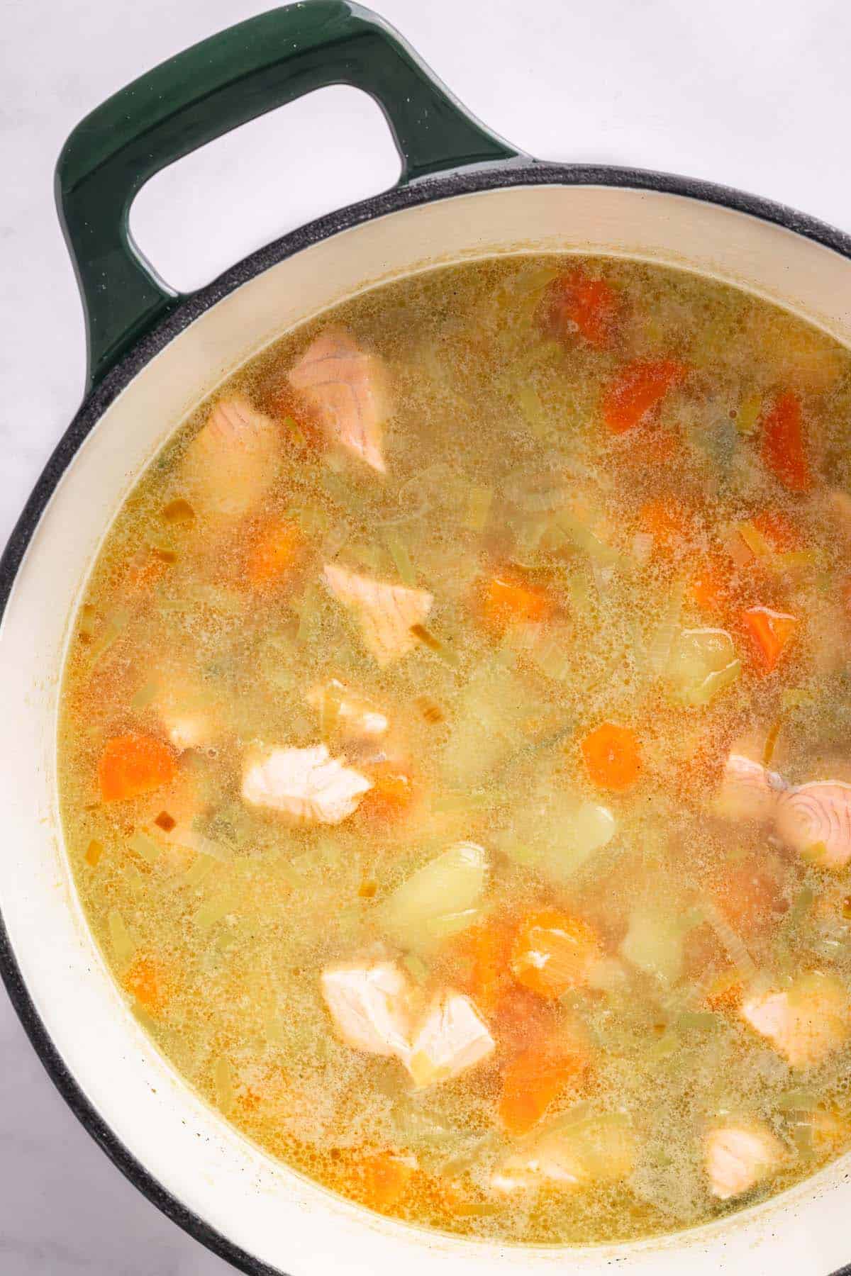 Salmon gently cooking with potatoes and vegetables in the broth.