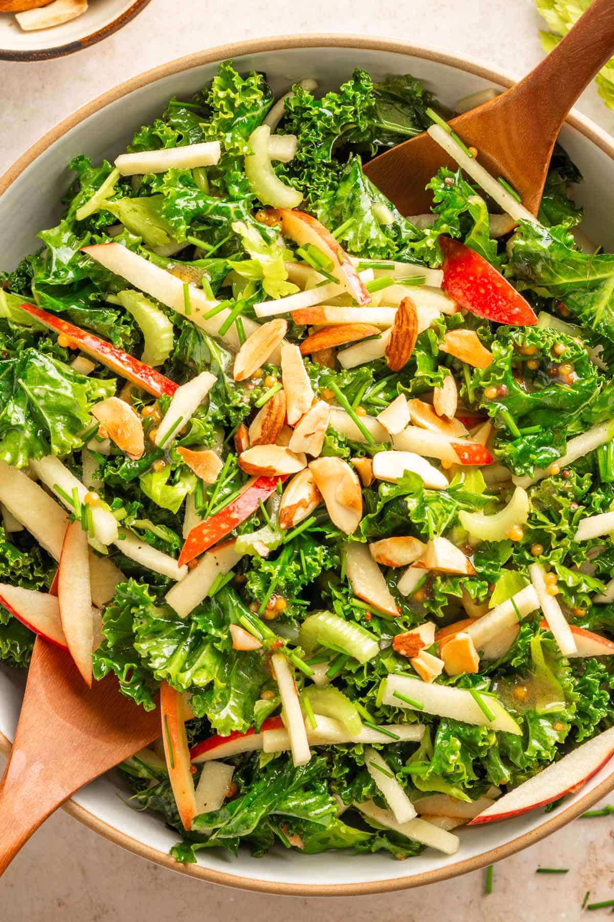Crunchy kale salad with apples, almonds, and miso mustard dressing in a serving bowl