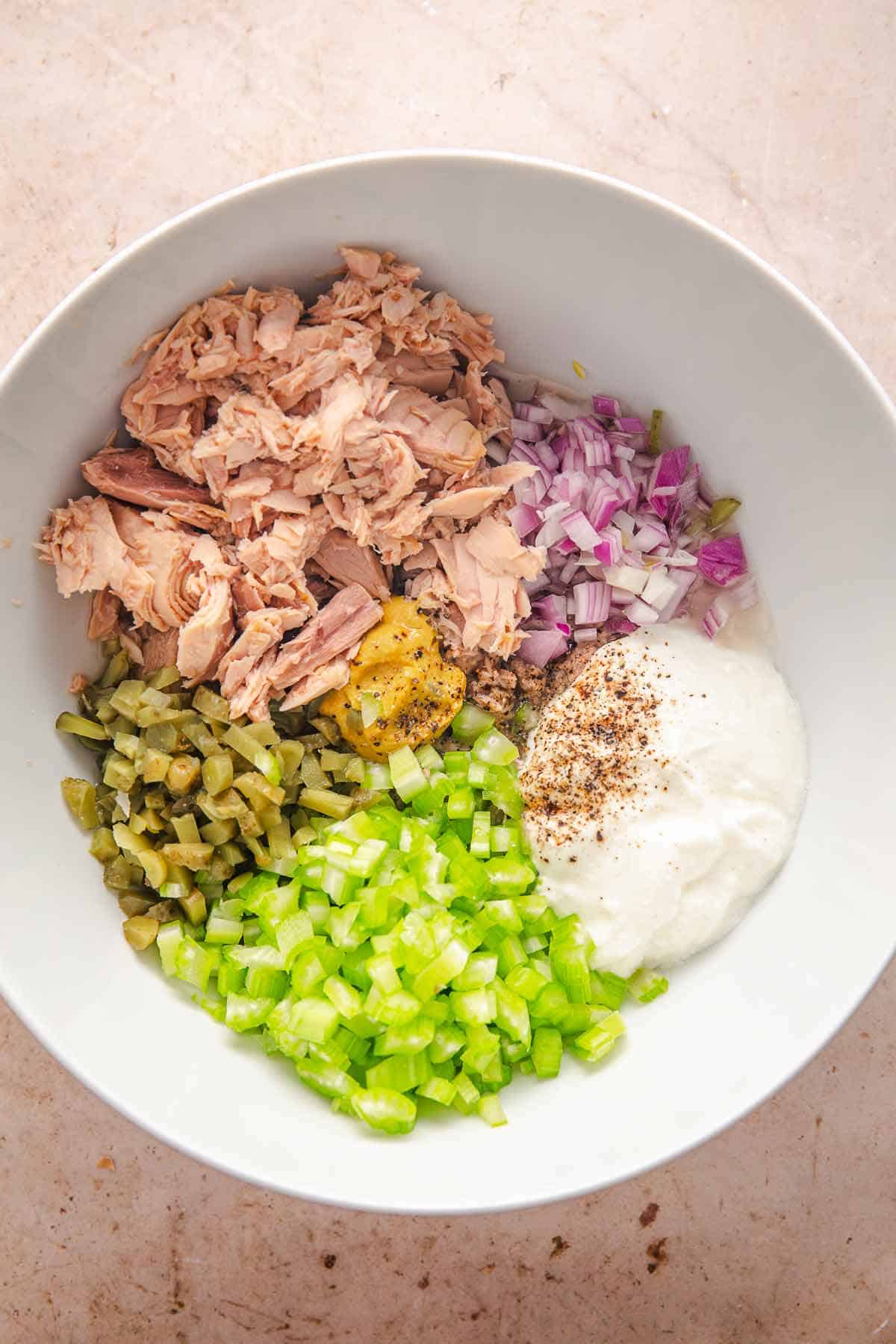 Bowl of tuna salad ingredients with celery, red onion, pickles, yogurt, and seasonings