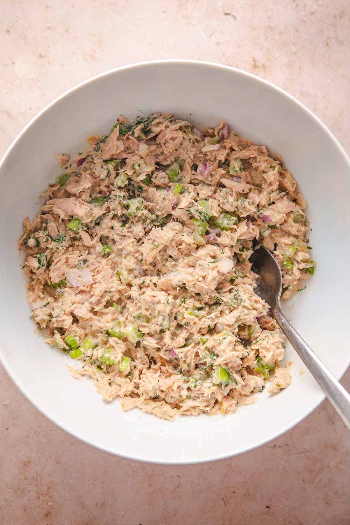 Creamy tuna salad mixed in a bowl with celery, red onion, dill, and a spoon