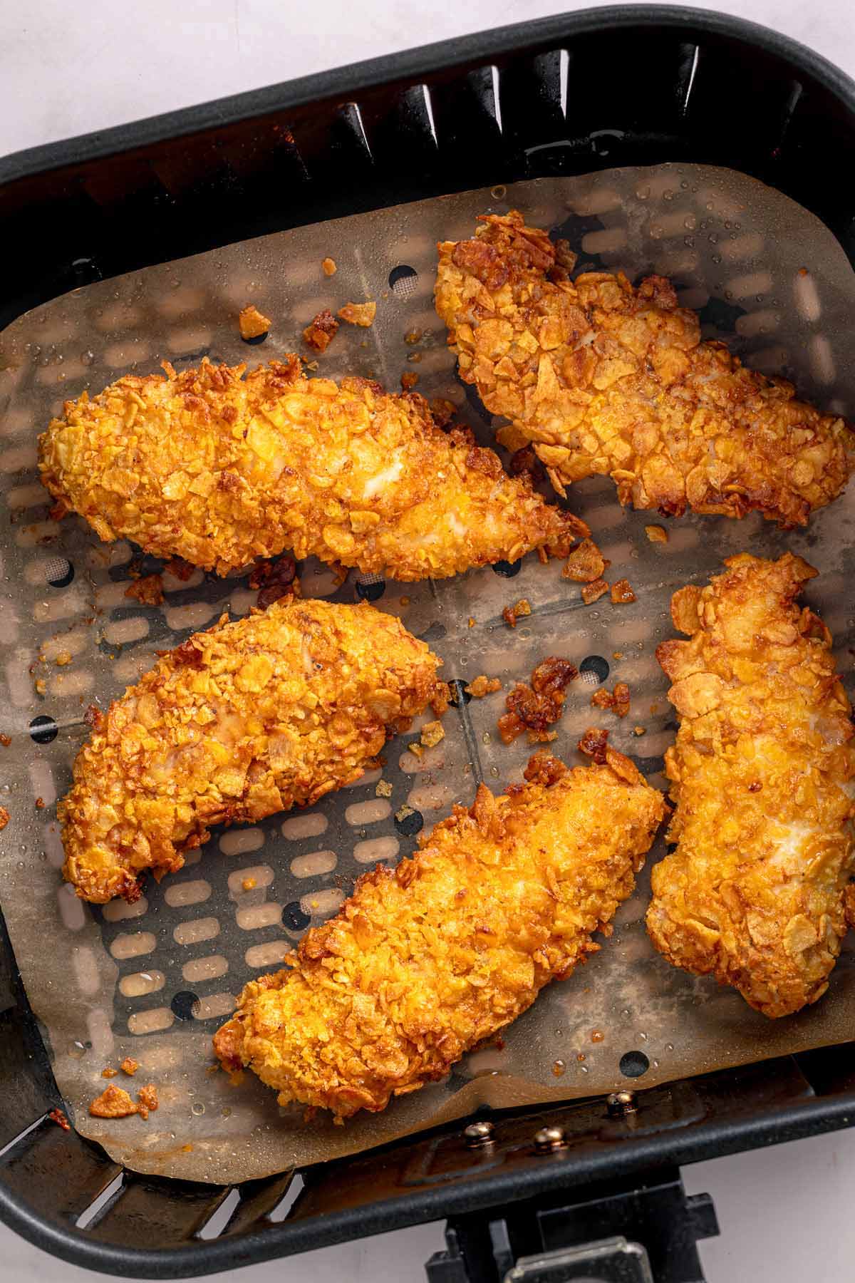 Golden cornflake chicken tenders cooking in an air fryer basket
