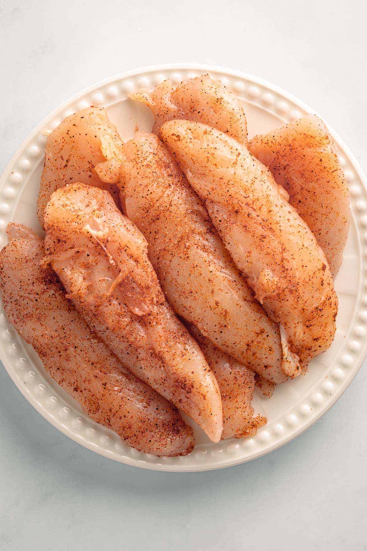 Raw seasoned chicken tenders in a white bowl