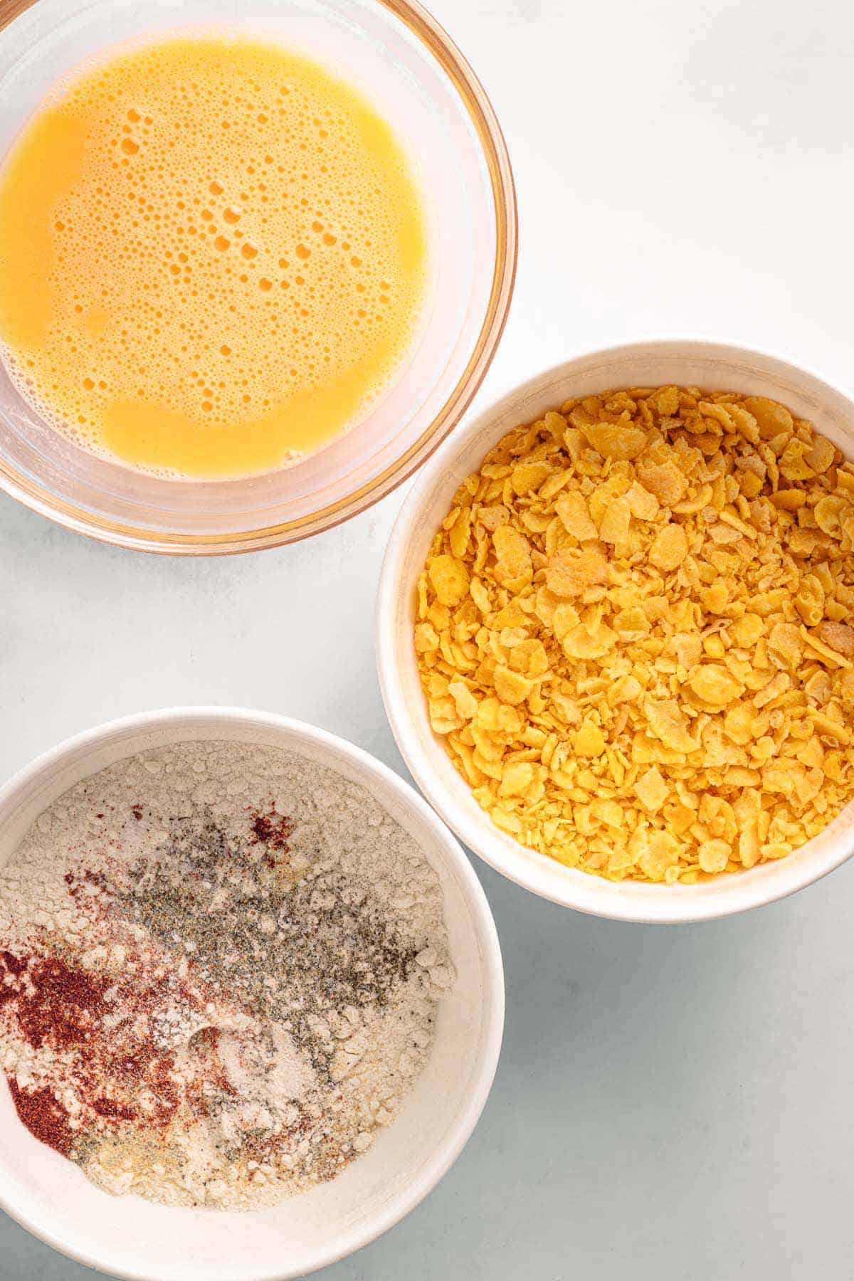 Bowls of beaten eggs, crushed cornflakes, and seasoned flour