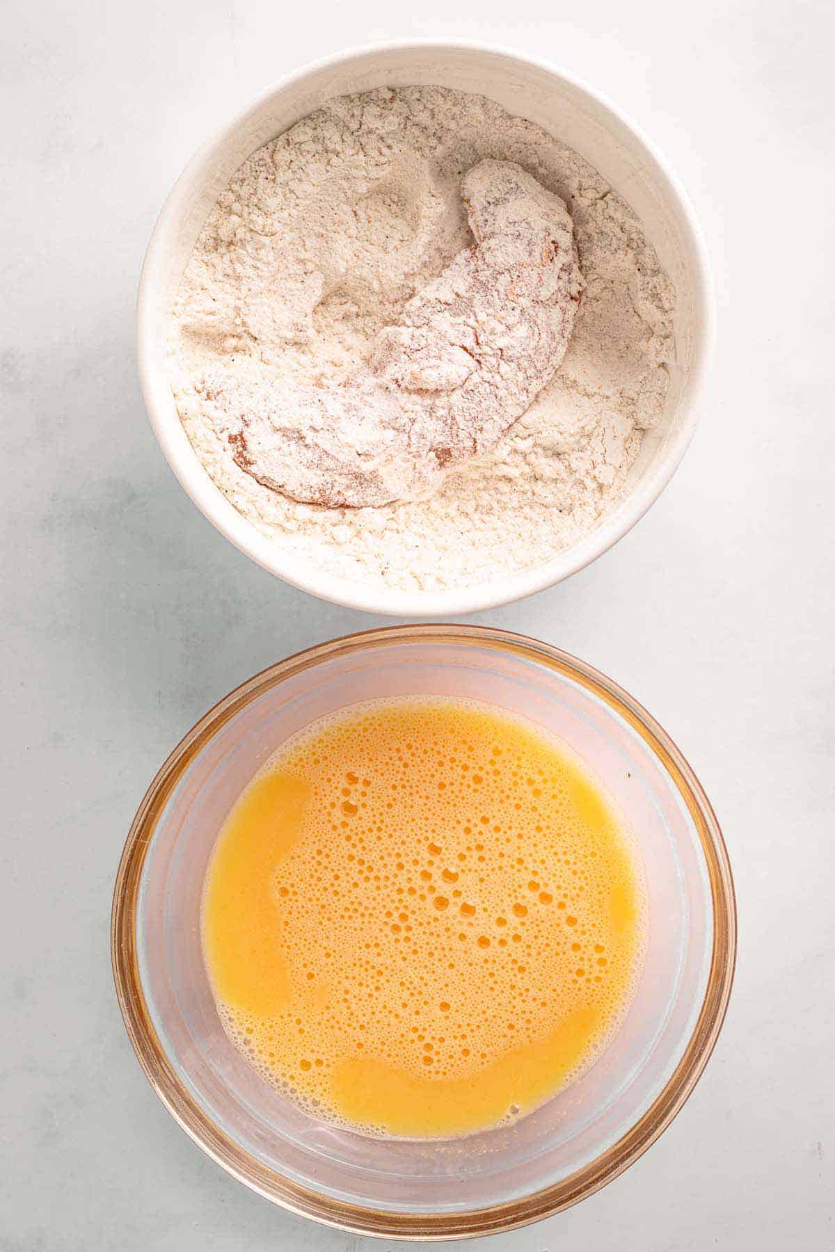 Chicken tender coated in flour above a bowl of beaten eggs
