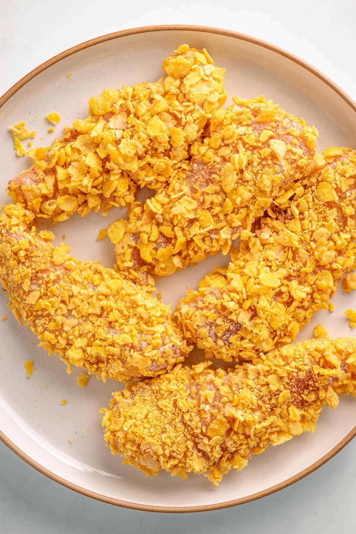 Cornflake-coated chicken tenders on a plate before cooking