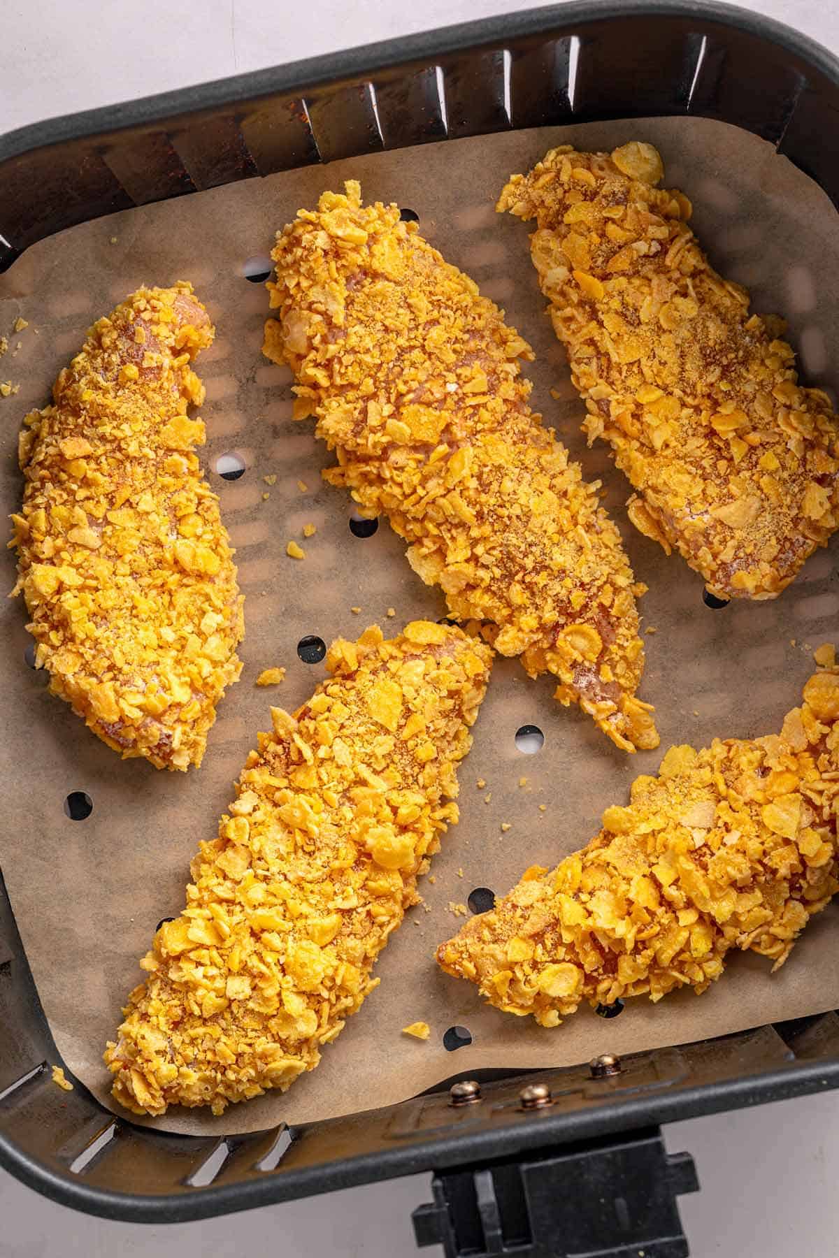 Breaded chicken tenders arranged in an air fryer basket before cooking