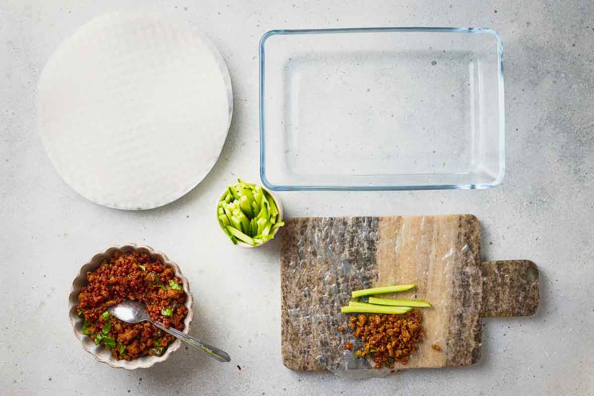 Ground beef filling and cucumber placed on softened rice paper for rolling.