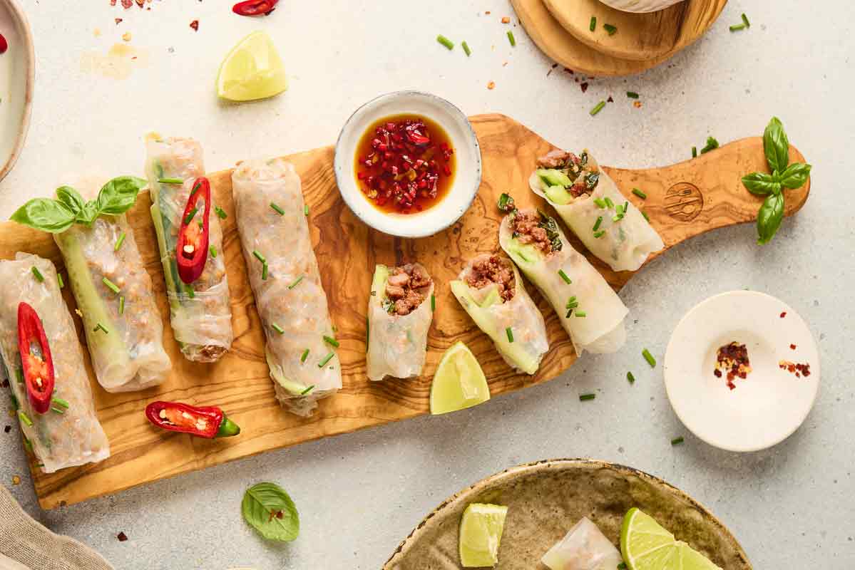 Thai-style ground beef spring rolls served with dipping sauce, lime, and fresh herbs.