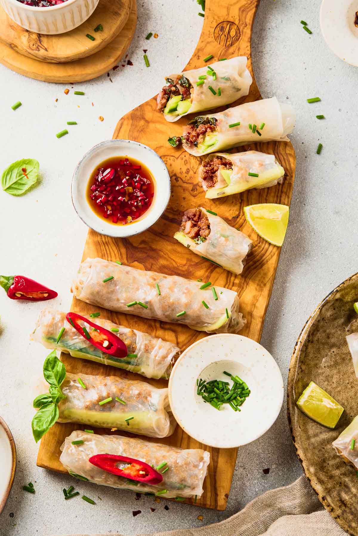 Ground beef spring rolls on a wooden board with dipping sauce and lime wedges.