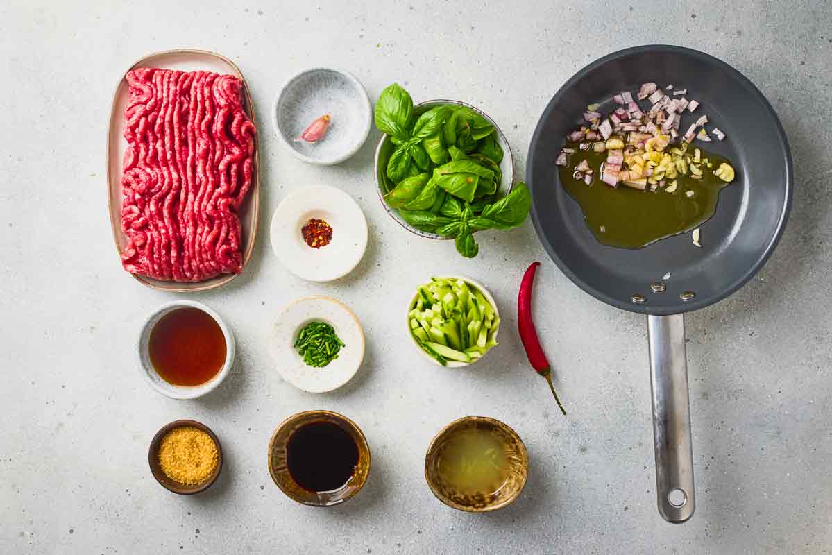 Garlic and shallot cooking in oil with ground beef and spring roll ingredients nearby.