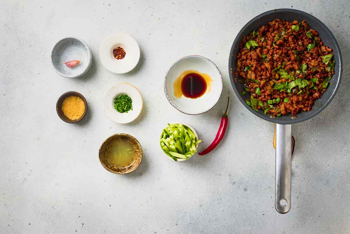 Thai basil mixed into the seasoned ground beef filling in a skillet.