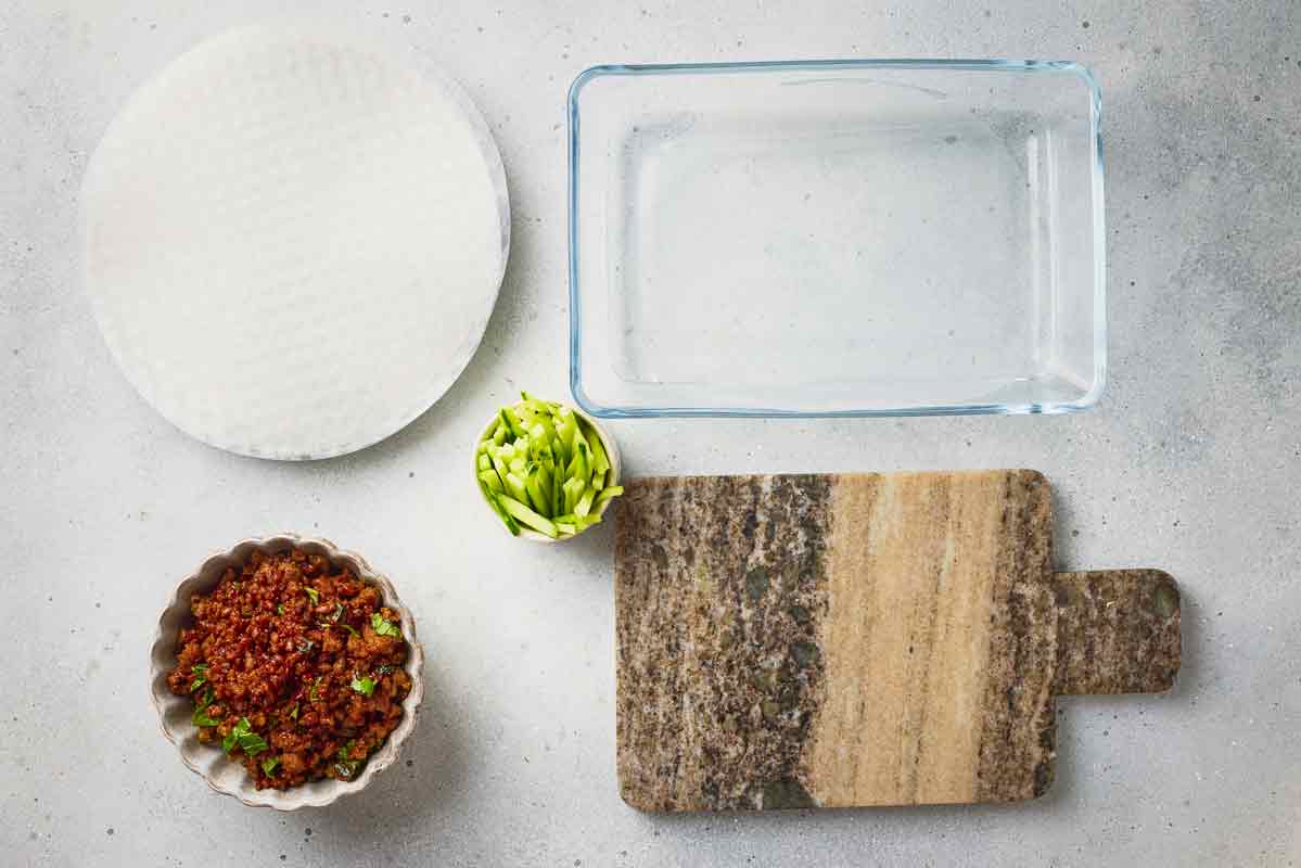 Rice paper wrappers, beef filling, cucumber, and warm water ready for rolling.