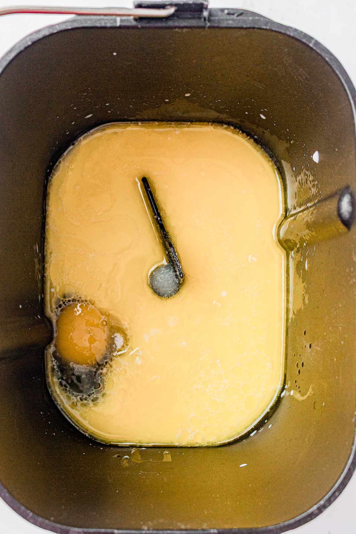 Bread machine pan with milk, egg, and butter before adding dry ingredients.