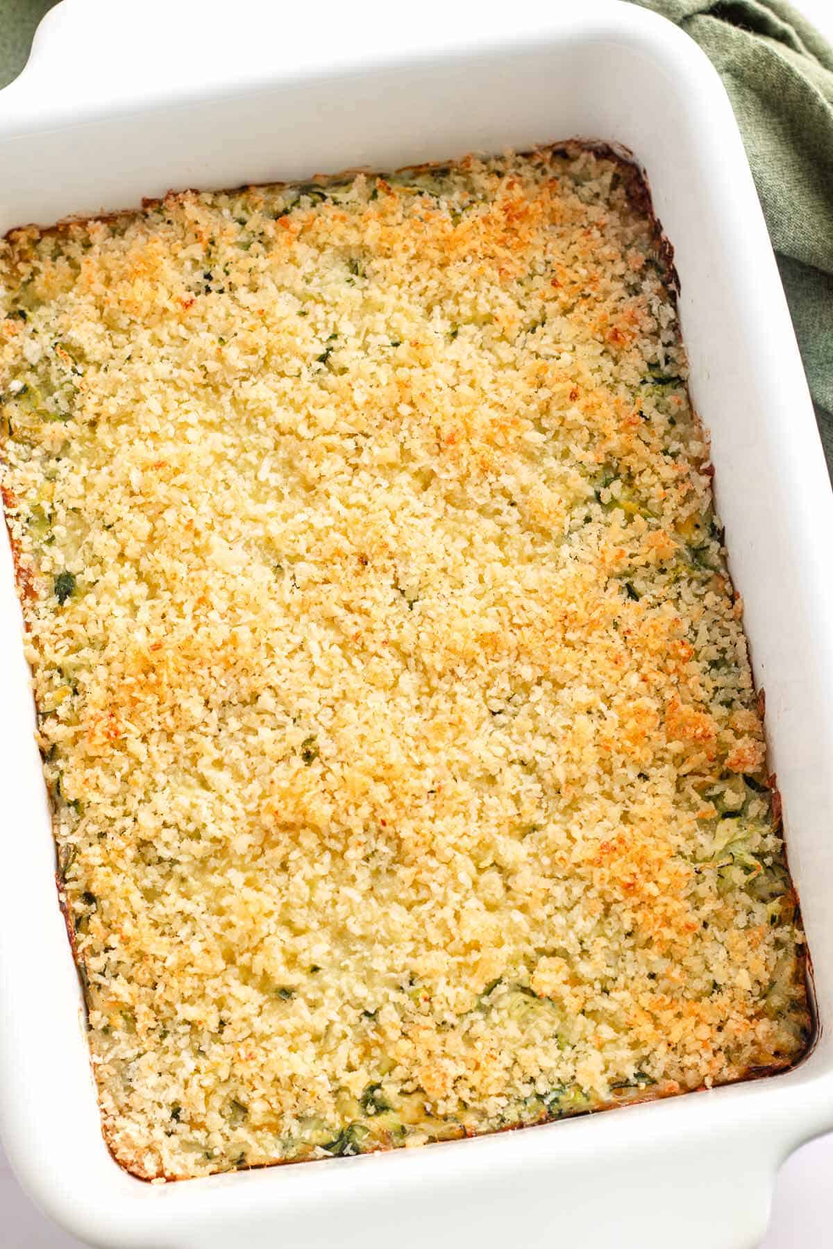 Serving spoon scooping cheesy zucchini casserole with a crispy breadcrumb topping