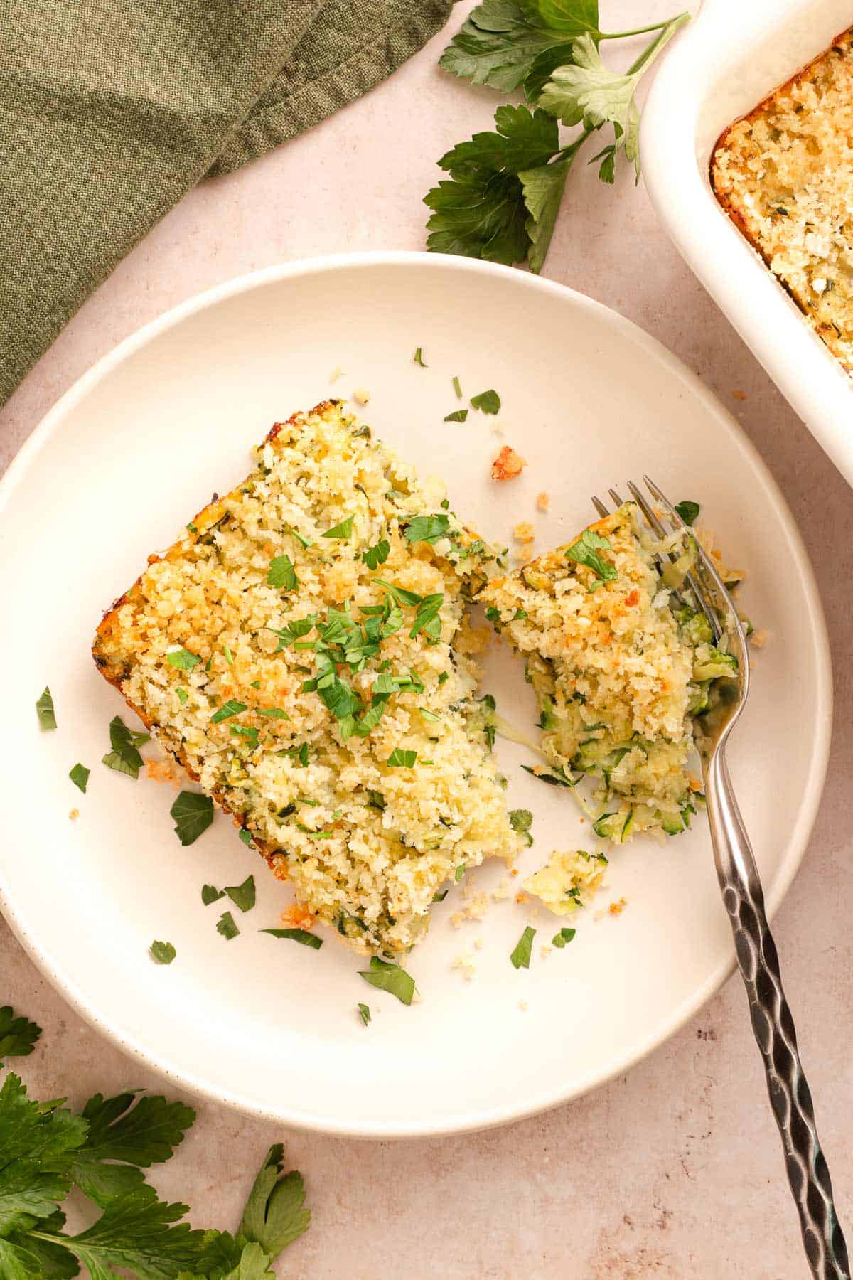 Slice of cheesy zucchini casserole on a plate with a crispy breadcrumb topping and parsley