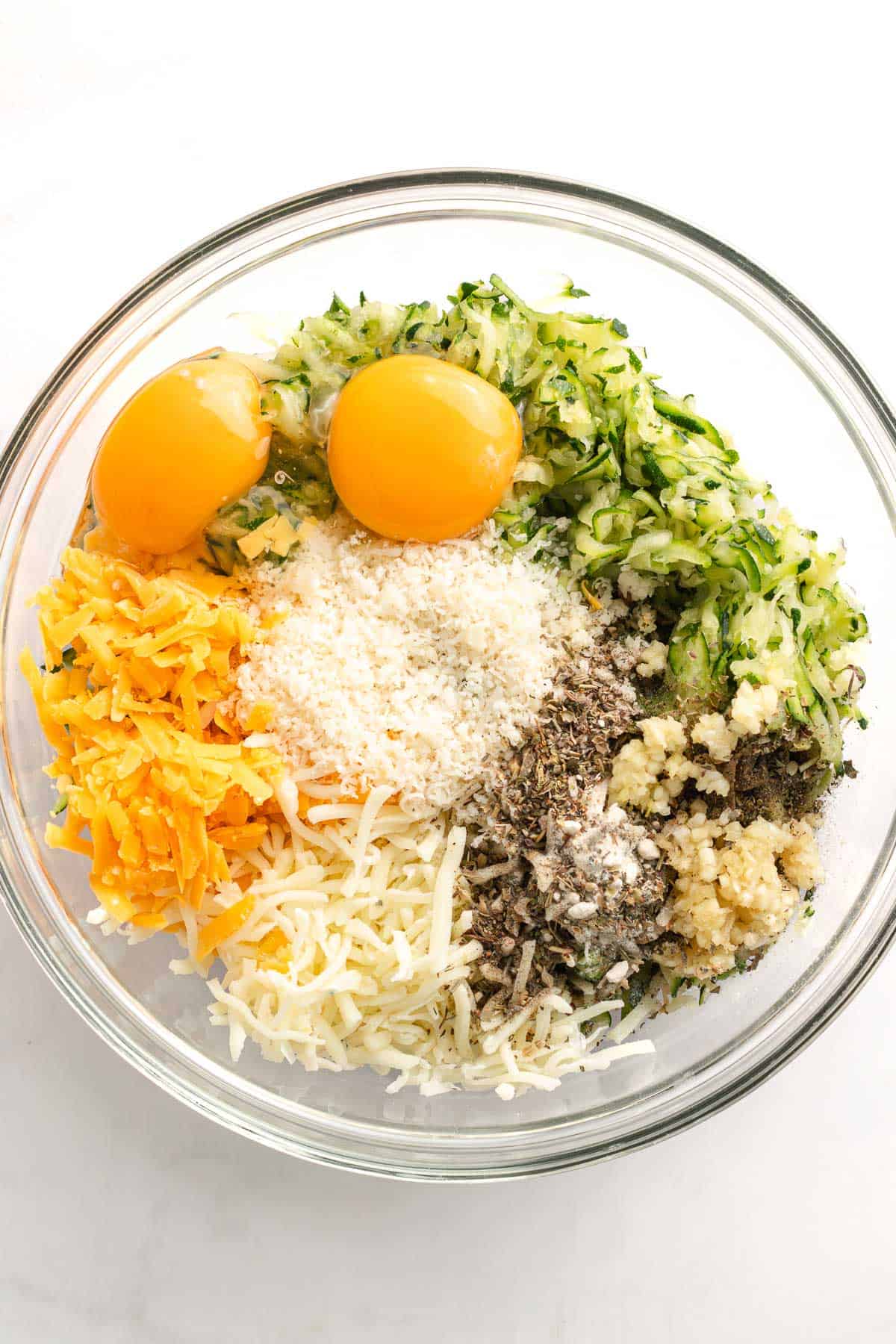 Grated zucchini, eggs, cheeses, garlic, and seasonings in a mixing bowl before stirring