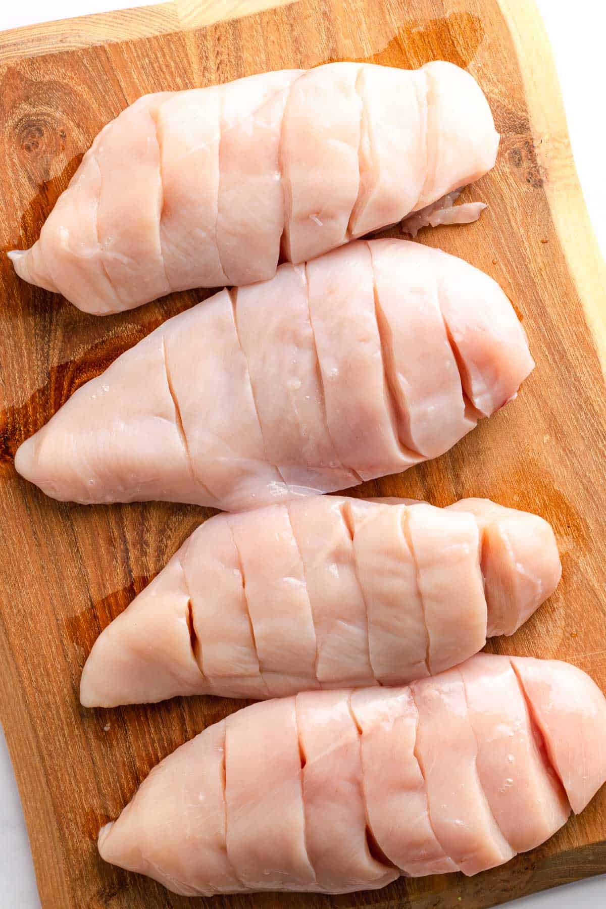Raw chicken breasts with hasselback cuts on a wooden cutting board