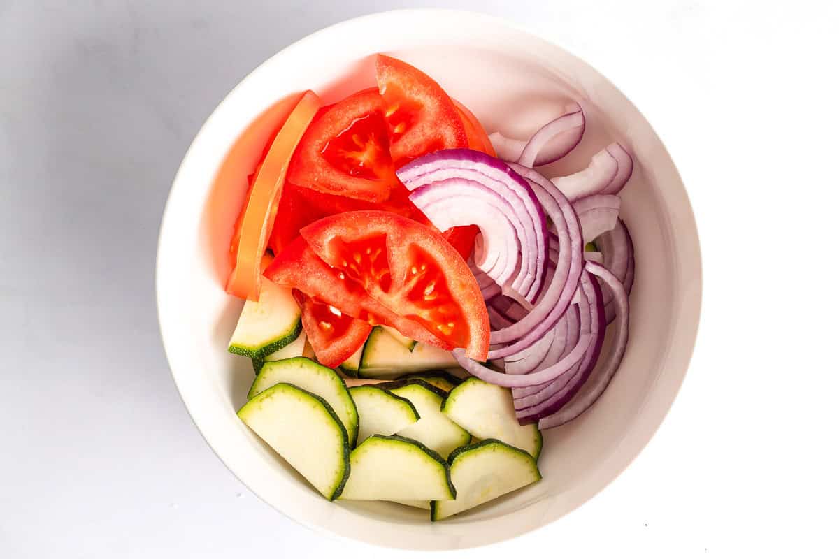 Sliced zucchini, tomato, and red onion in a white bowl