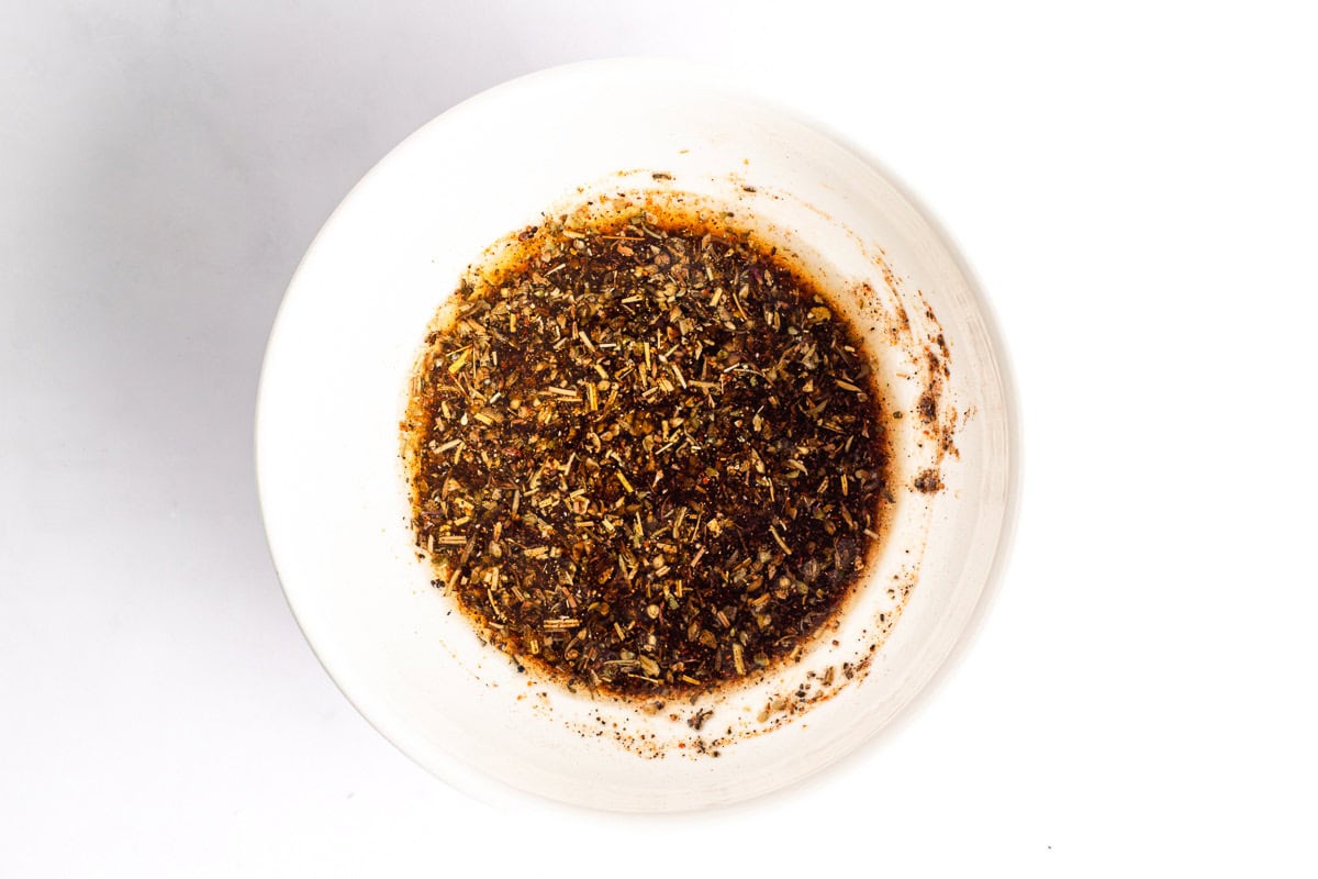 Olive oil mixed with Italian herbs and seasonings in a white bowl
