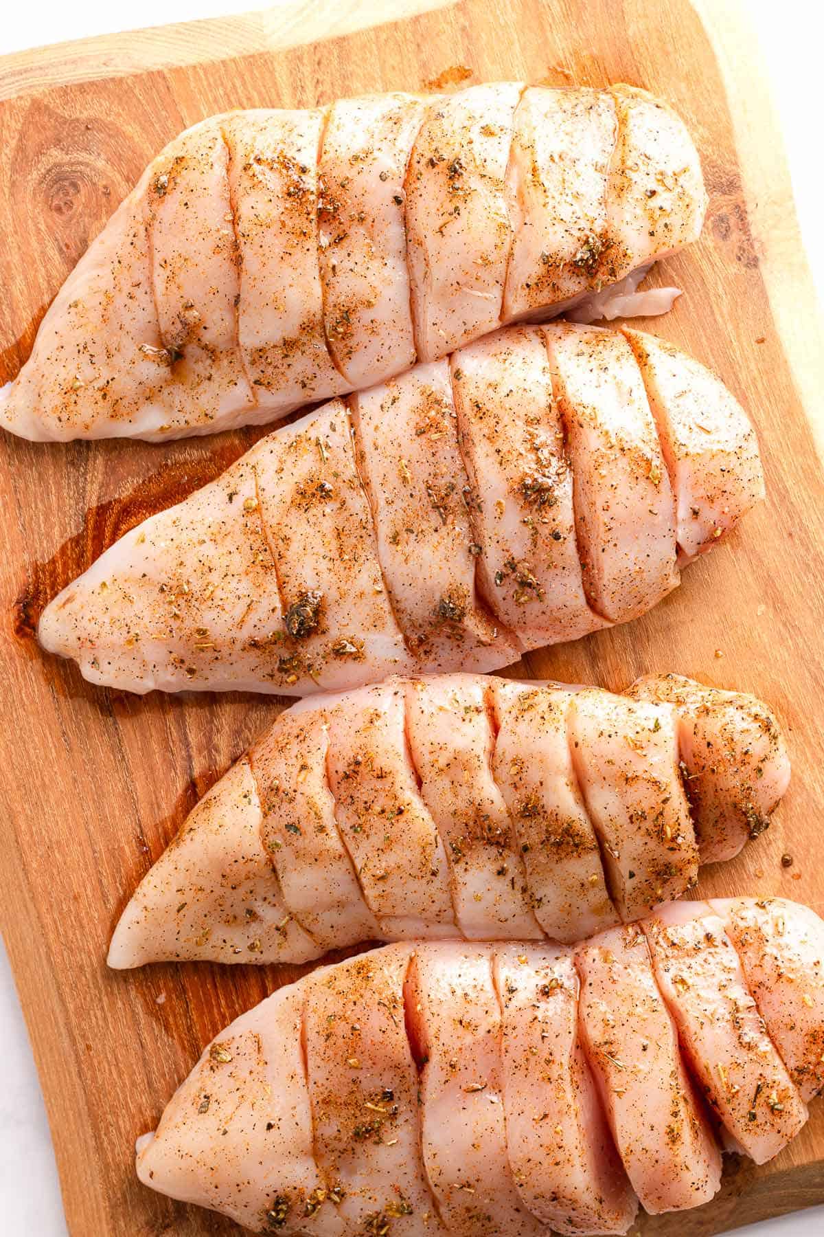 Seasoned hasselback chicken breasts on a wooden cutting board