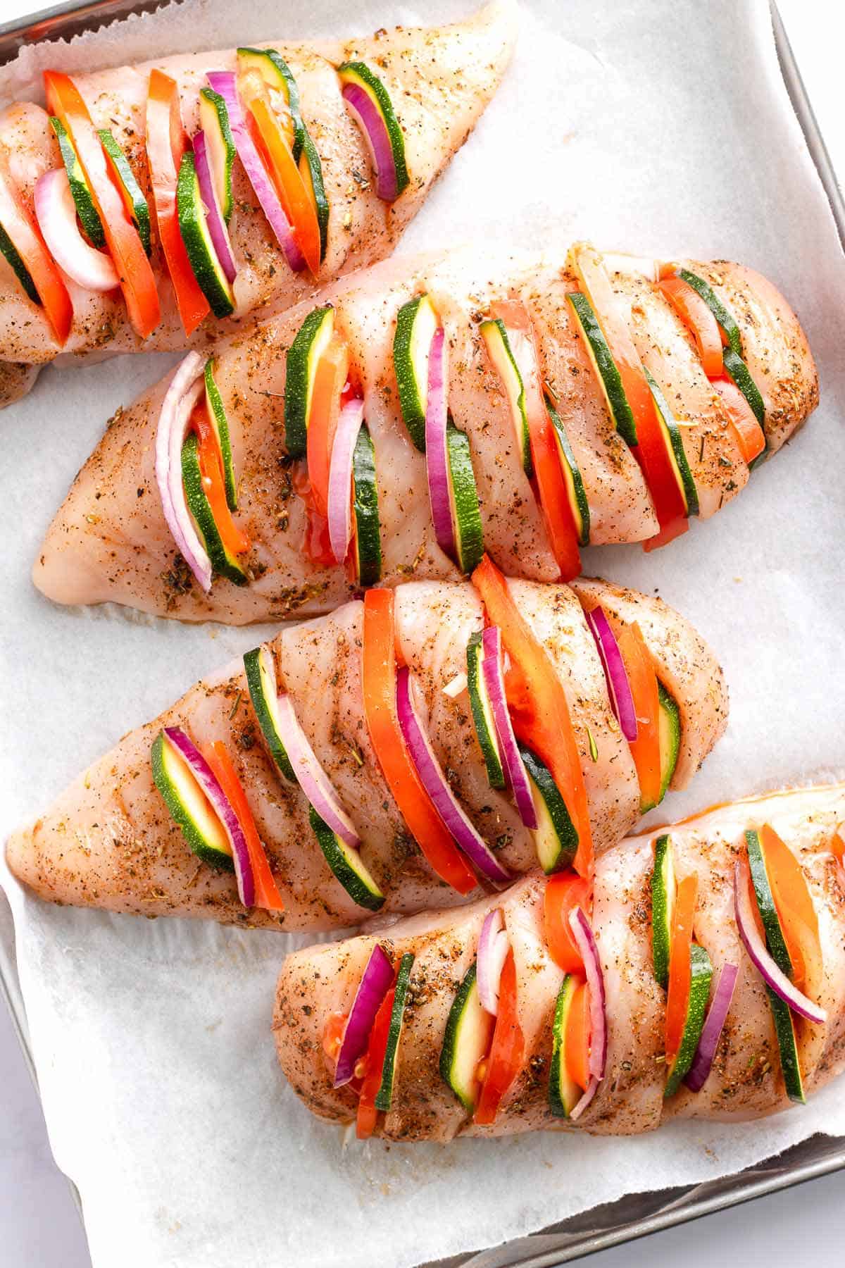 Chicken breasts stuffed with zucchini, tomato, and red onion on a sheet pan