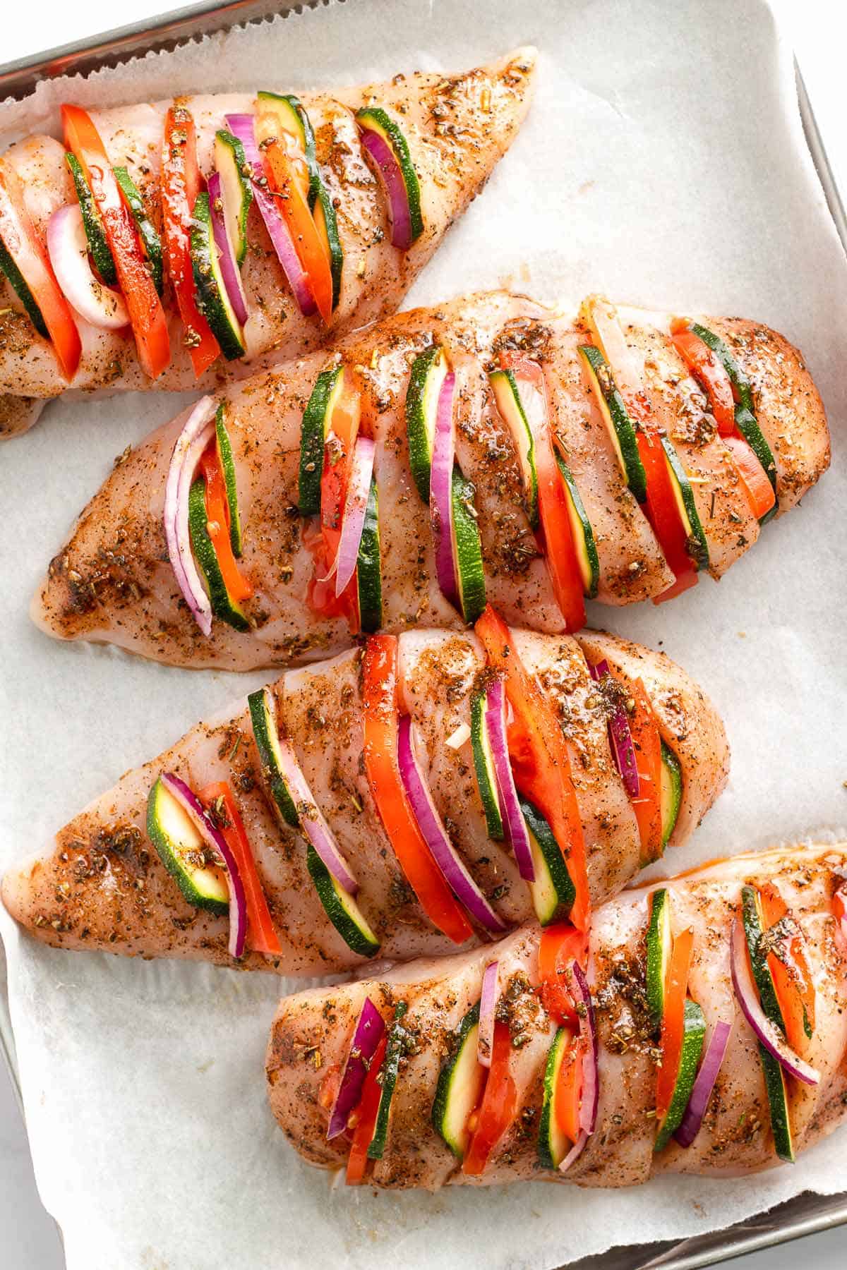 Stuffed hasselback chicken breasts arranged on a parchment-lined baking sheet