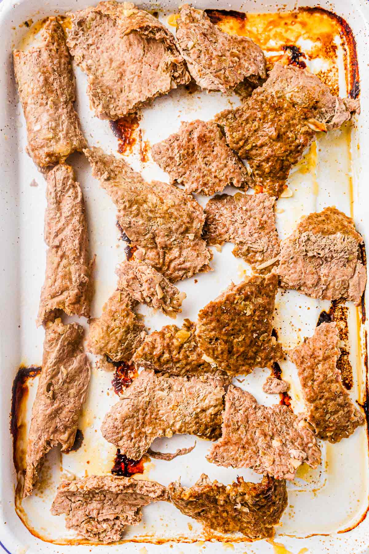 Cooked kebab meat sliced into thin pieces on a baking tray