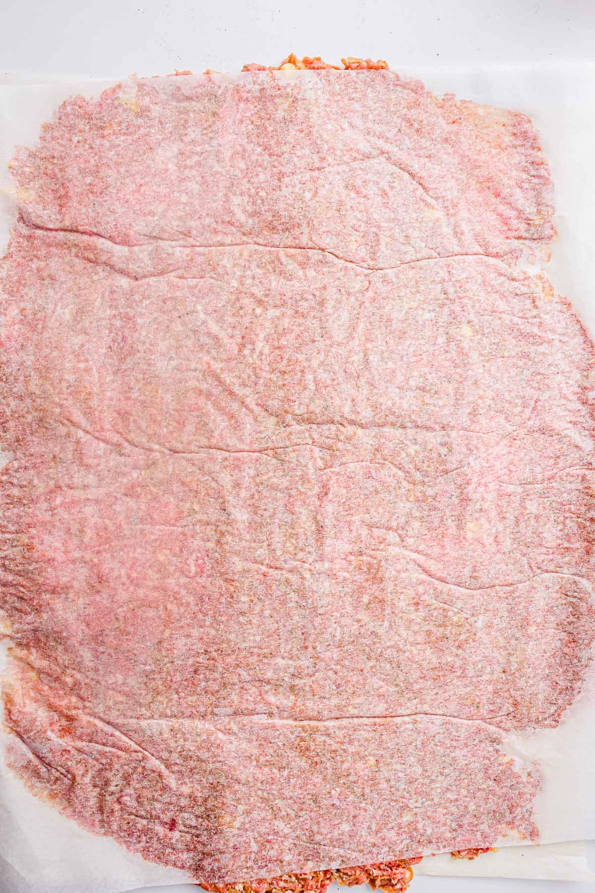 Seasoned meat rolled into a thin, even rectangle between parchment paper