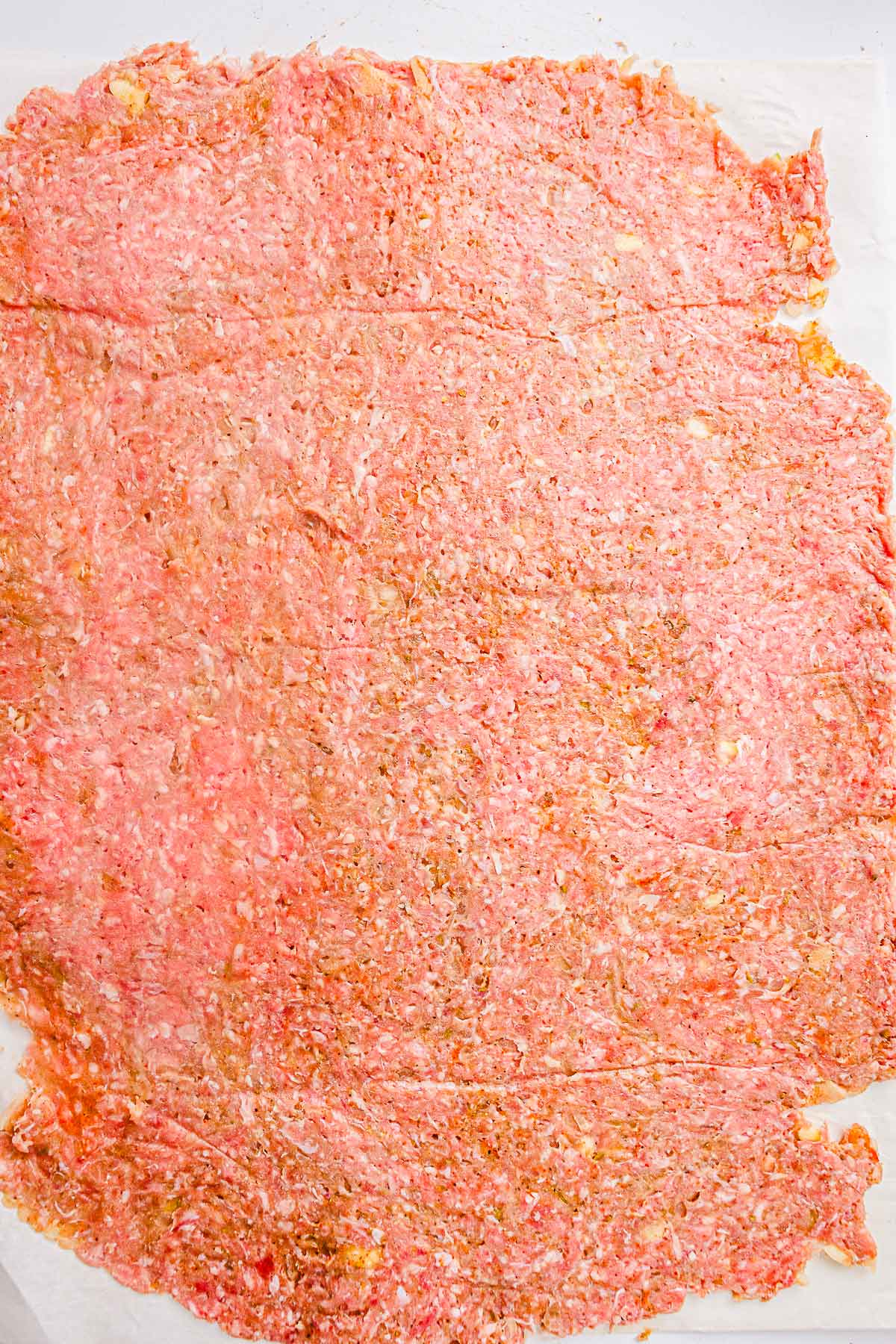 Seasoned ground meat rolled into a thin, even rectangle on parchment paper