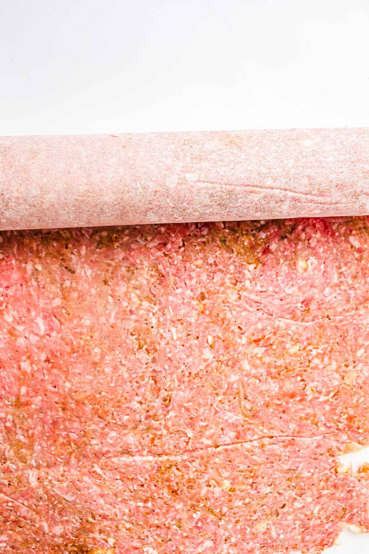 Rolling pin flattening seasoned ground meat between parchment paper