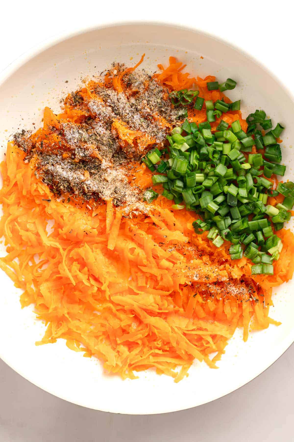 Grated sweet potato with green onions and seasonings in a bowl