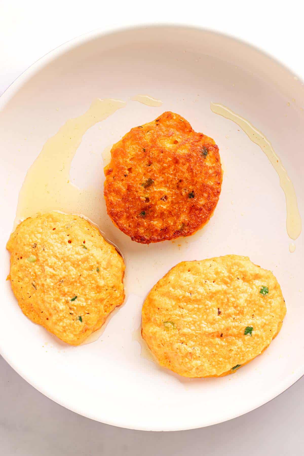 Three uncooked red lentil fritters cooking in a skillet