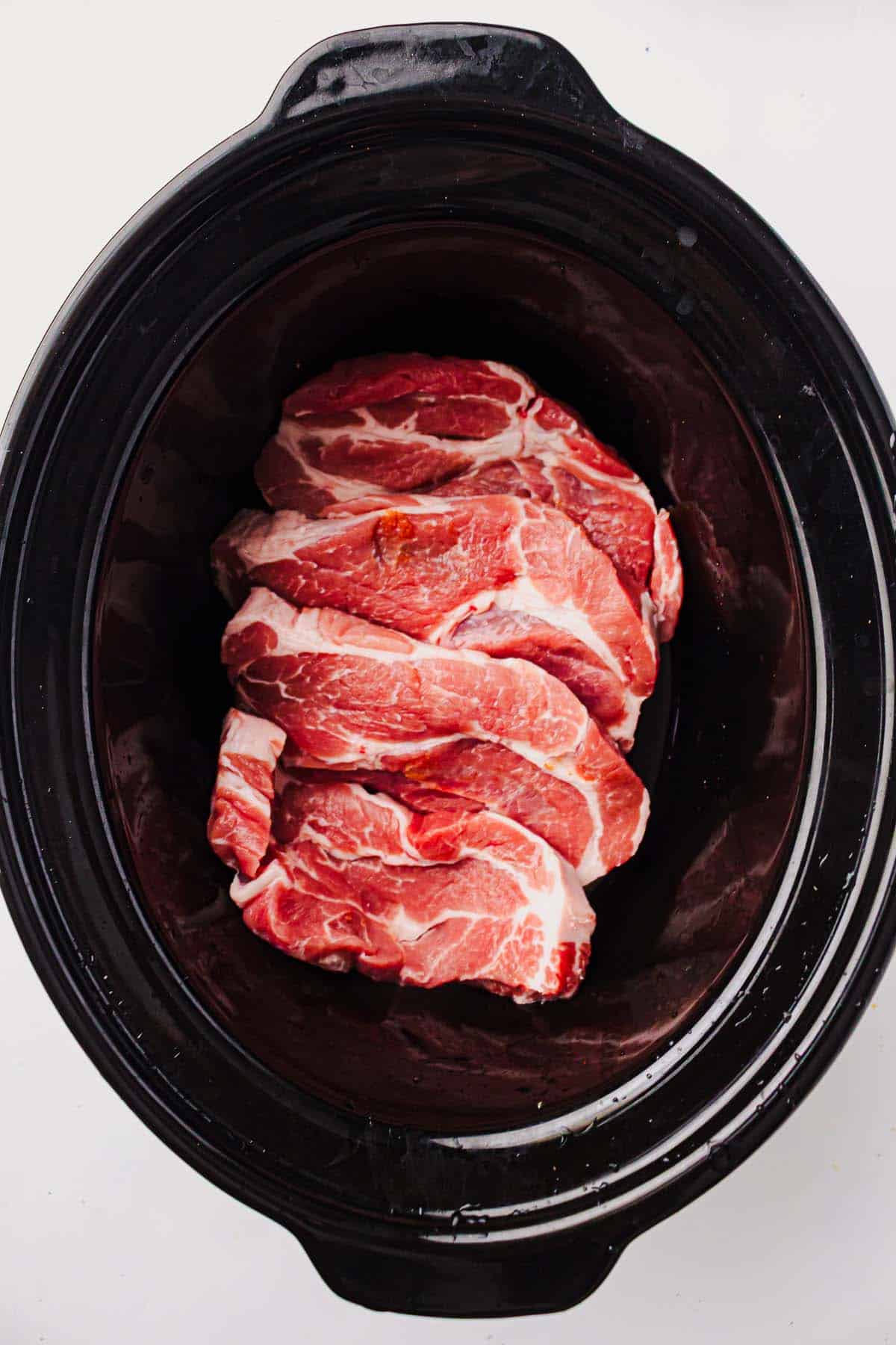 Raw pork shoulder steaks arranged in a slow cooker