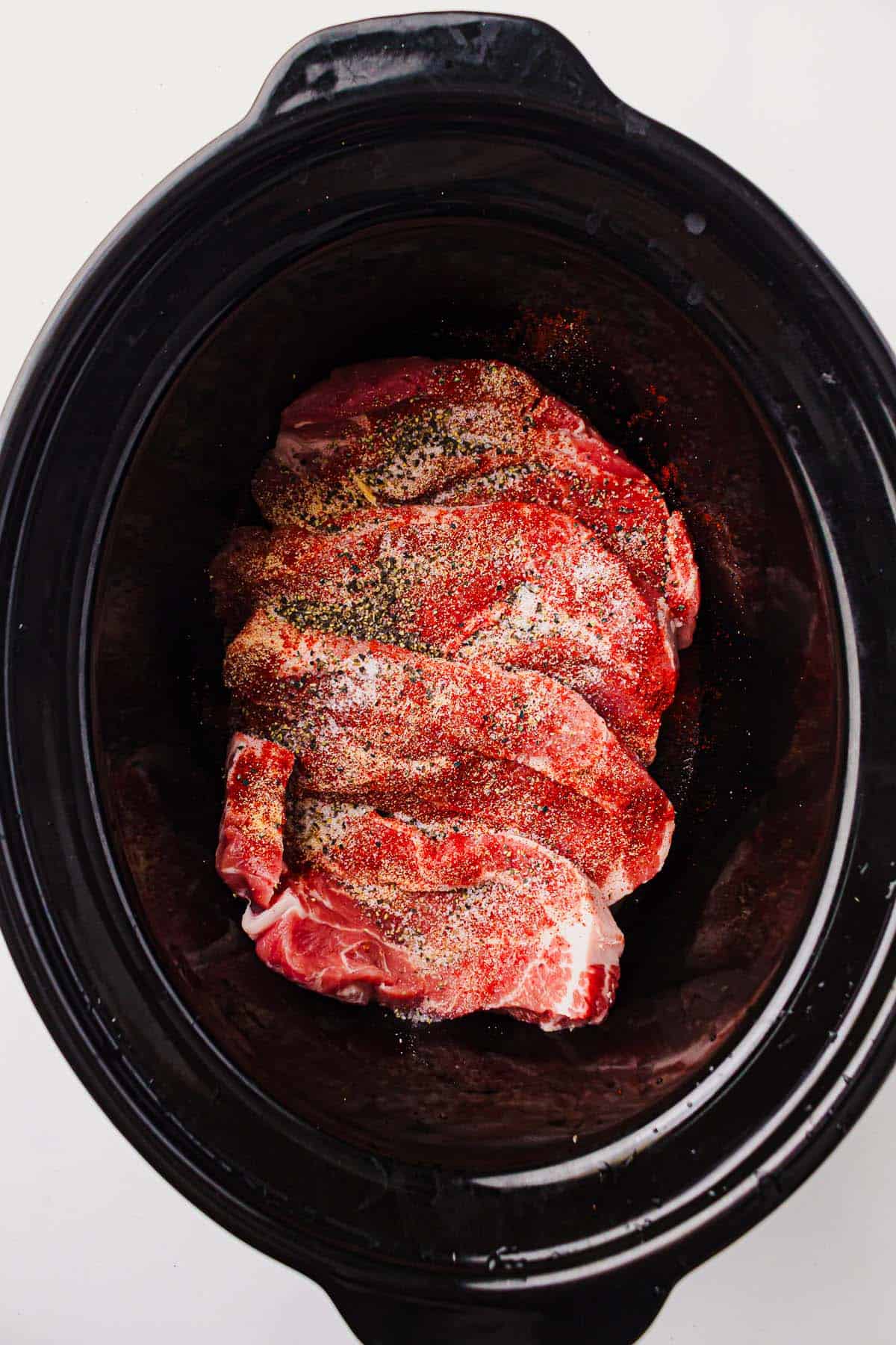 Seasoned pork shoulder steaks in a slow cooker before cooking