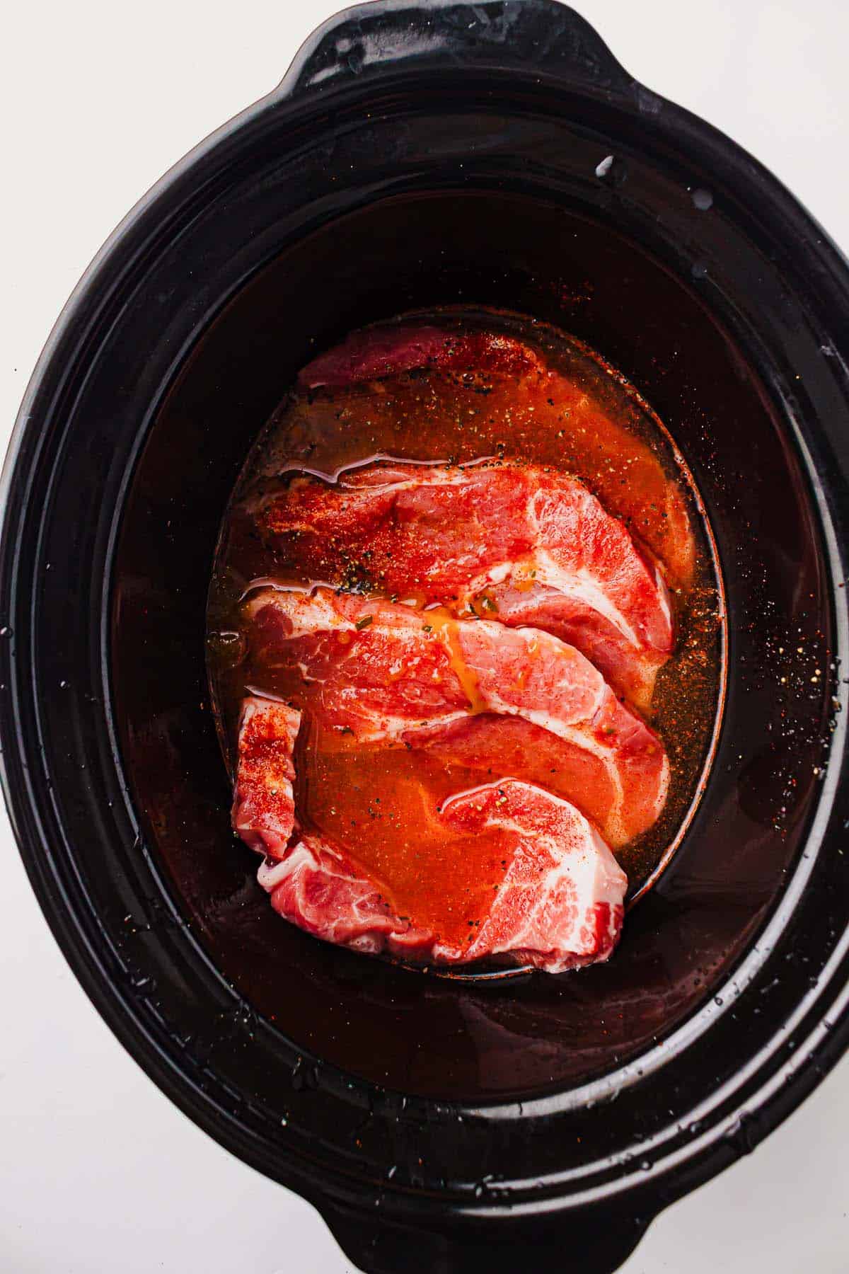 Pork shoulder with broth and seasonings in a slow cooker