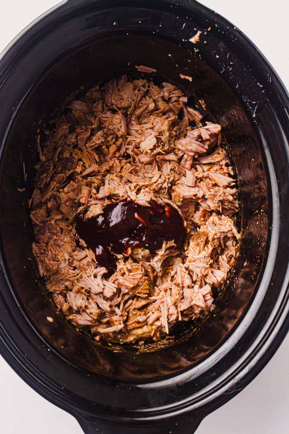 BBQ sauce added to shredded pulled pork in a slow cooker