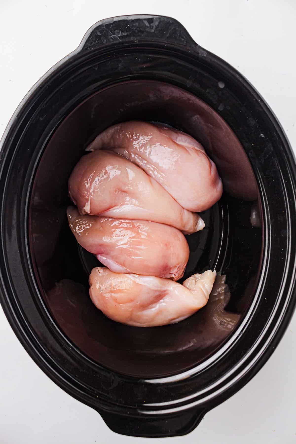 Raw chicken breasts placed in a slow cooker before seasoning.