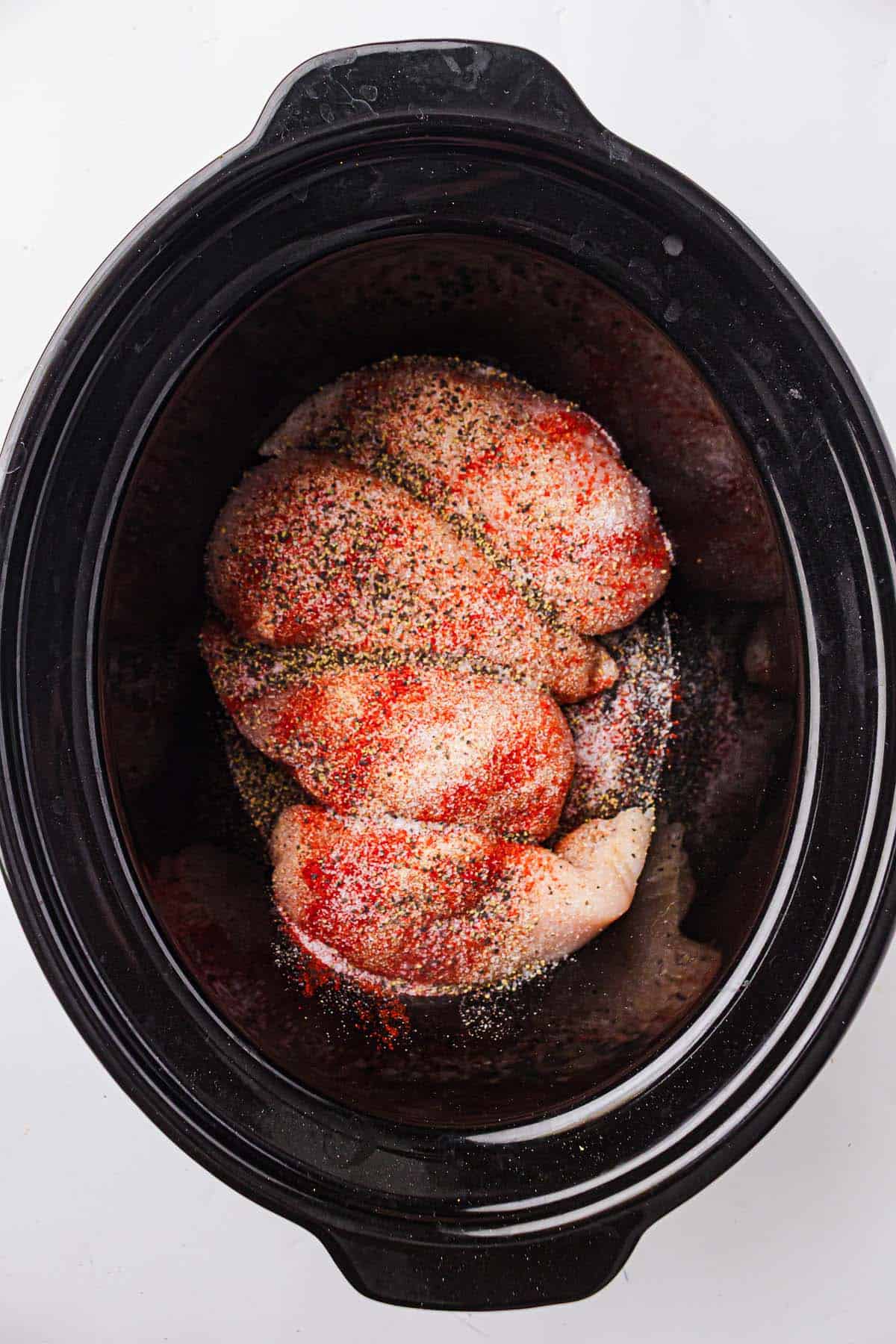 Chicken breasts seasoned with spices in a slow cooker.