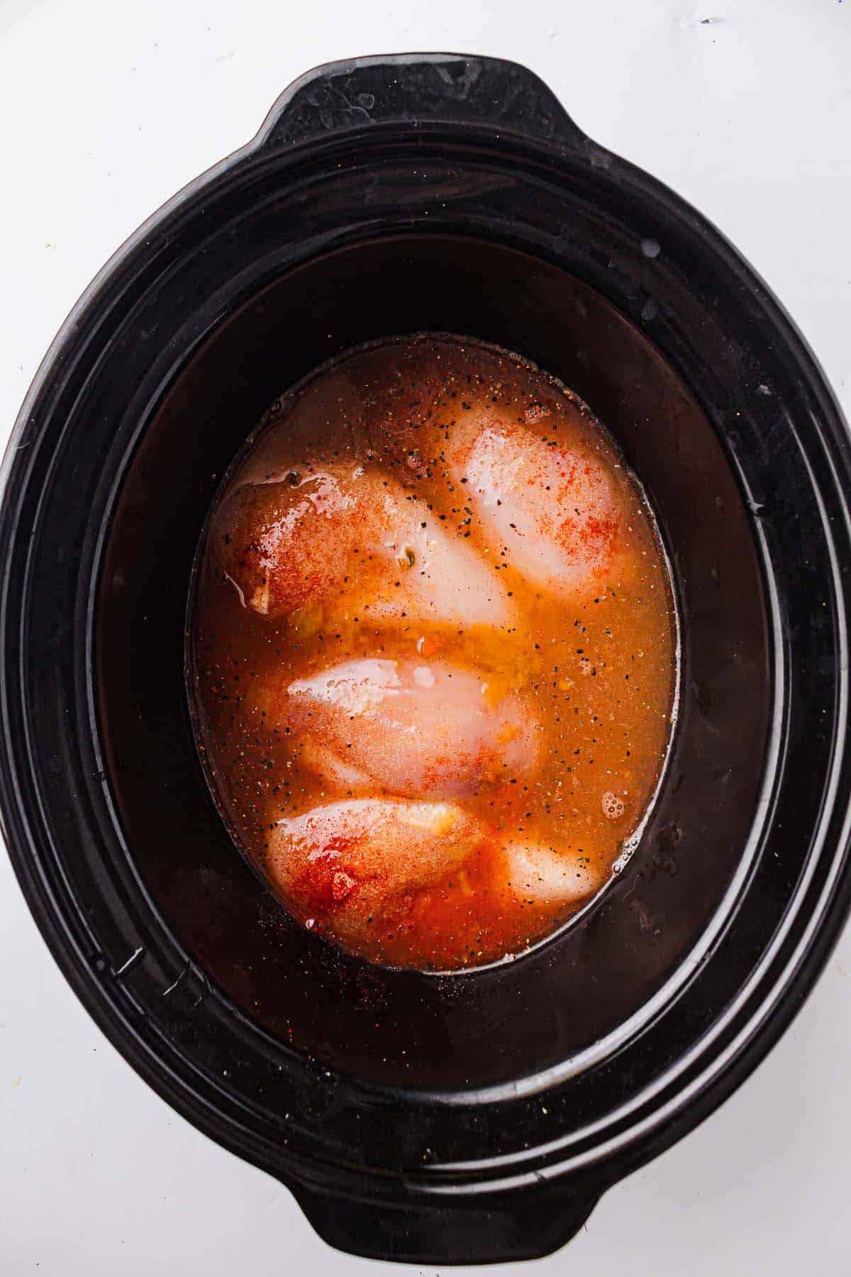 Chicken breasts covered with broth and seasonings in a slow cooker.