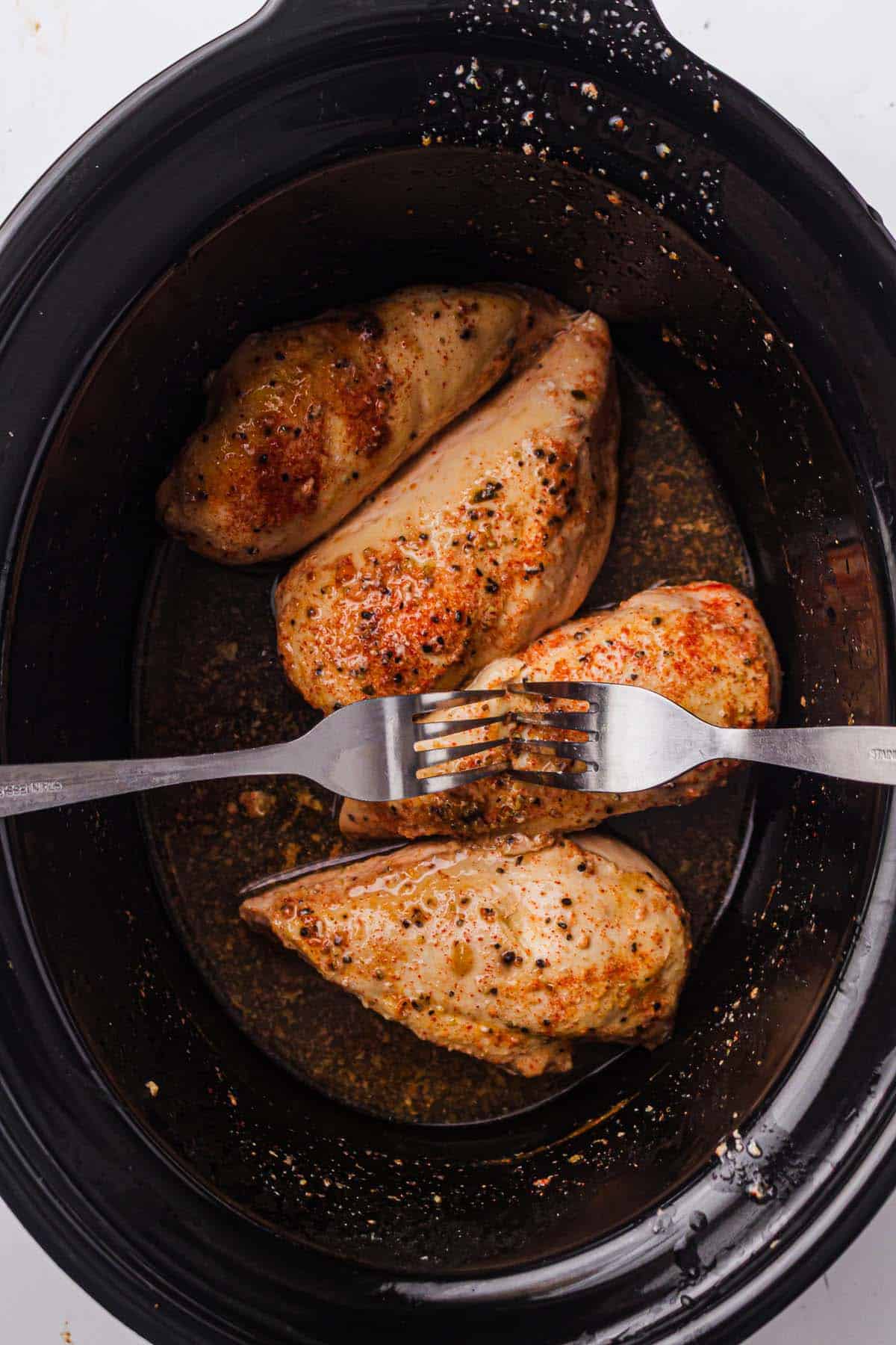 Fork shredding cooked chicken in a slow cooker.