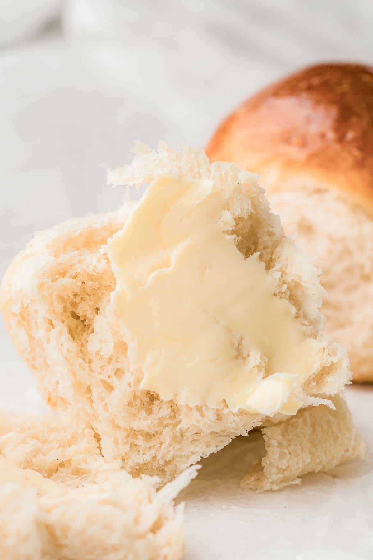 Fluffy dinner roll split open and spread with butter.