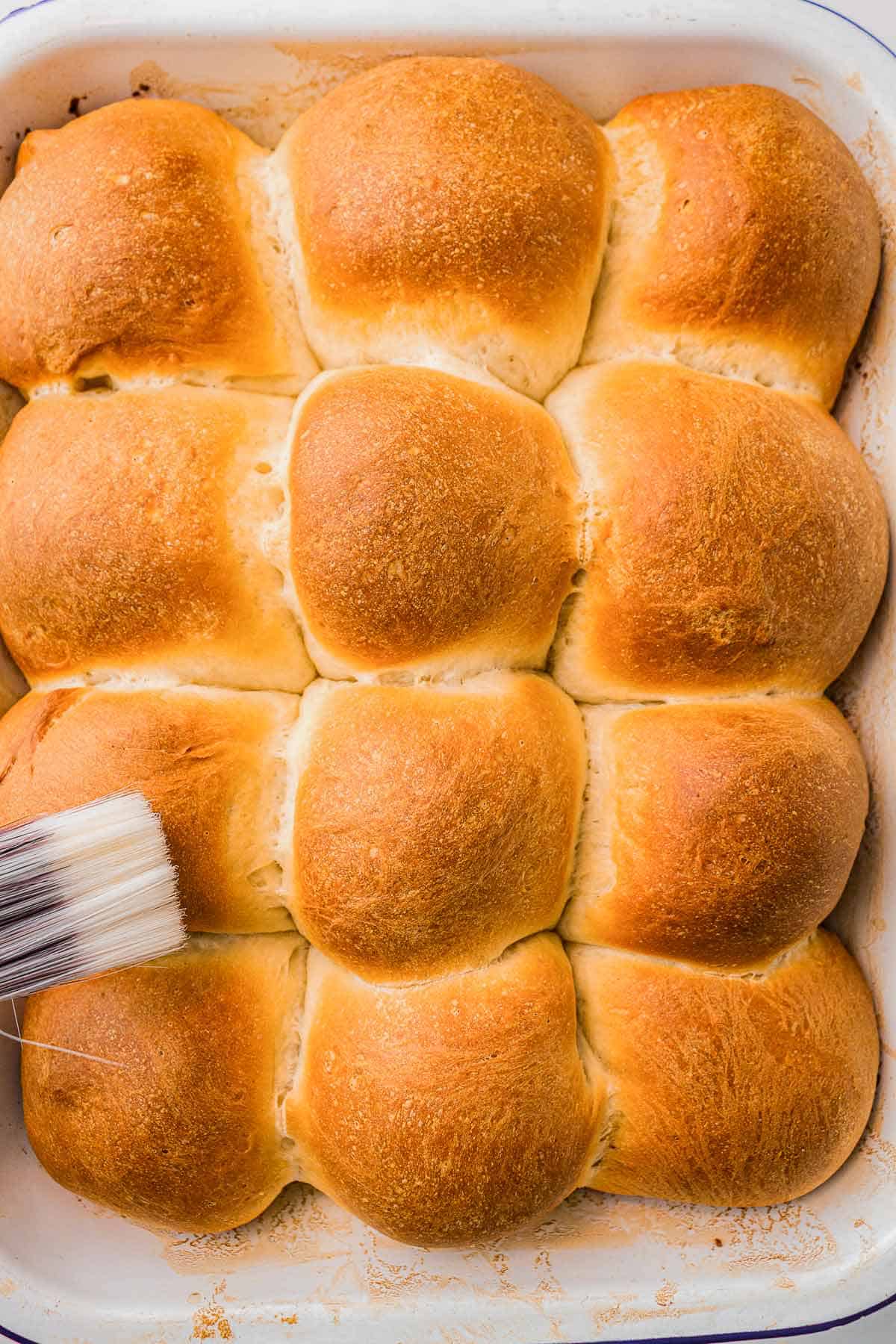 Brushing melted butter over warm homemade dinner rolls.